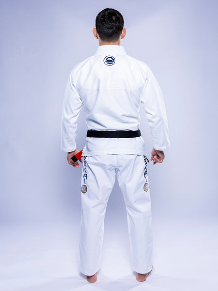 A person stands barefoot, facing away in the SEKAI 3.0 BJJ Gi White Navy with a black belt. The gi features patches on sleeves and pants, set against a plain light-colored background.