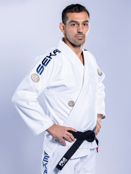 A man stands confidently with hands on hips, wearing the SEKAI 3.0 BJJ Gi White Navy and a black belt, looking at the camera against a plain light background.