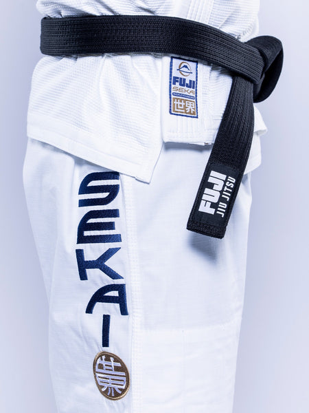 Close-up of a person wearing the SEKAI 3.0 BJJ Gi White Navy with blue Sekai lettering, a black belt, and Fuji brand patches on both the gi and the belt.