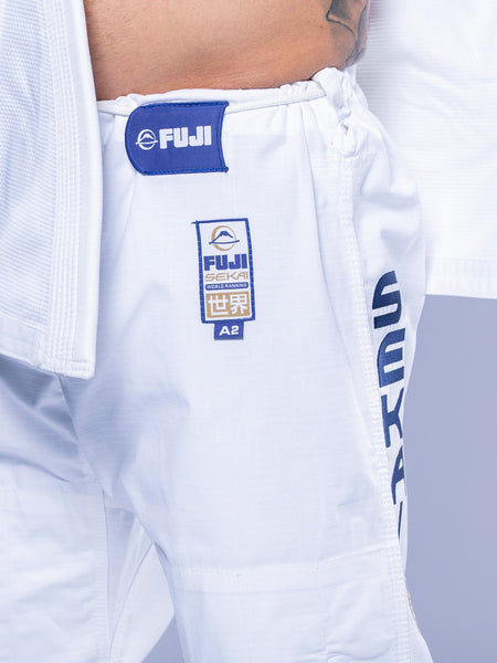 Close-up of a person wearing SEKAI 3.0 BJJ Gi White Navy pants with an A2 size label, blue and gold logo, and "SEKAI" text on the side, as part of a martial arts uniform.